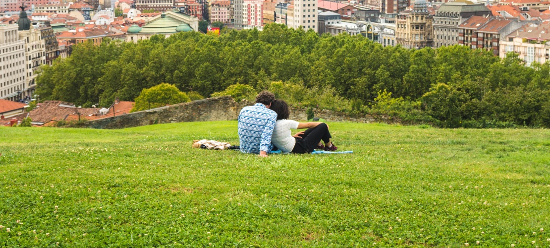 Pareja viendo una hermosa vista panorámica de Bilbao sentada en el parque de la colina sobre el Casco Antiguo Pareja viendo una hermosa vista panorámica de Bilbao sentada en el parque de la colina sobre el Casco Antiguo
