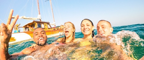 Junge Leute schwimmen bei einem Segelboot auf Ibiza Junge Leute schwimmen bei einem Segelboot auf Ibiza