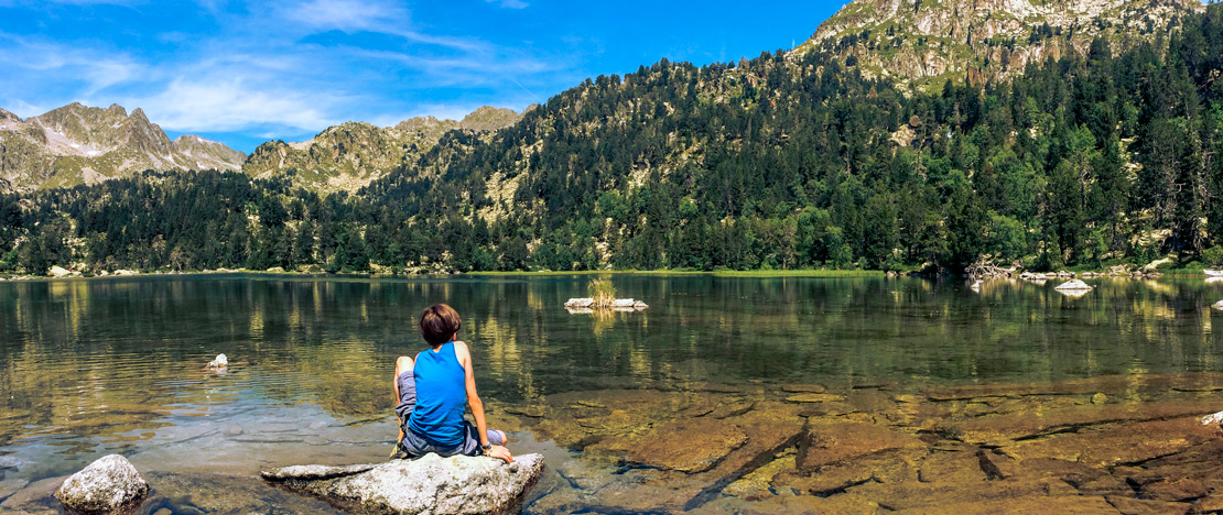 Niño sentado en uno de los lagos del Parque Nacional de Aigüestortes i Estany de Sant Maurici en Lérida, Cataluña Niño sentado en uno de los lagos del Parque Nacional de Aigüestortes i Estany de Sant Maurici en Lérida, Cataluña